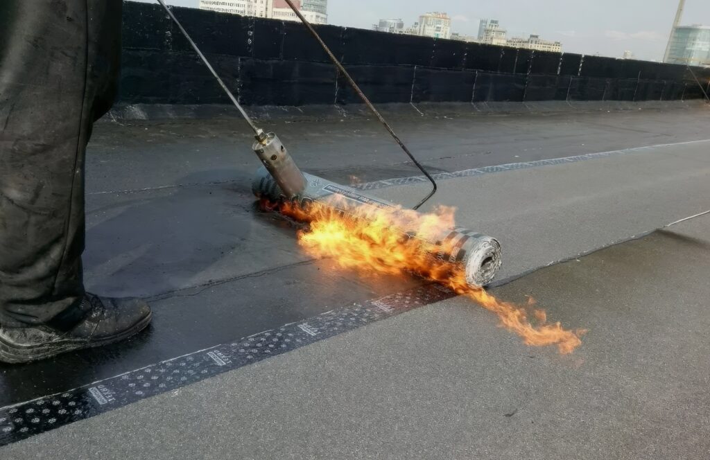 Proces de termosudare a membranei bituminoase folosind un arzător cu flacără, showing flacăra în timpul aplicării