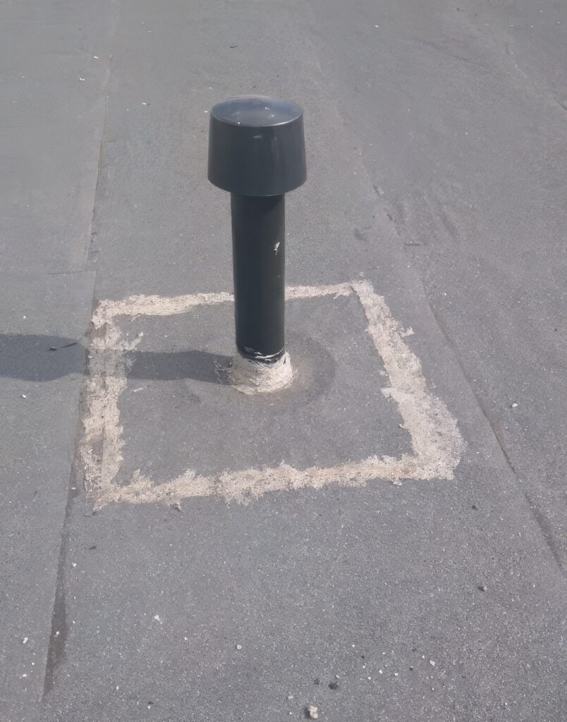 Aerisitor negru de acoperiș instalat într-un petic pătrat de membrană bituminoasă